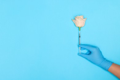 Doctor making injection to rose on light blue background, top view. Space for text