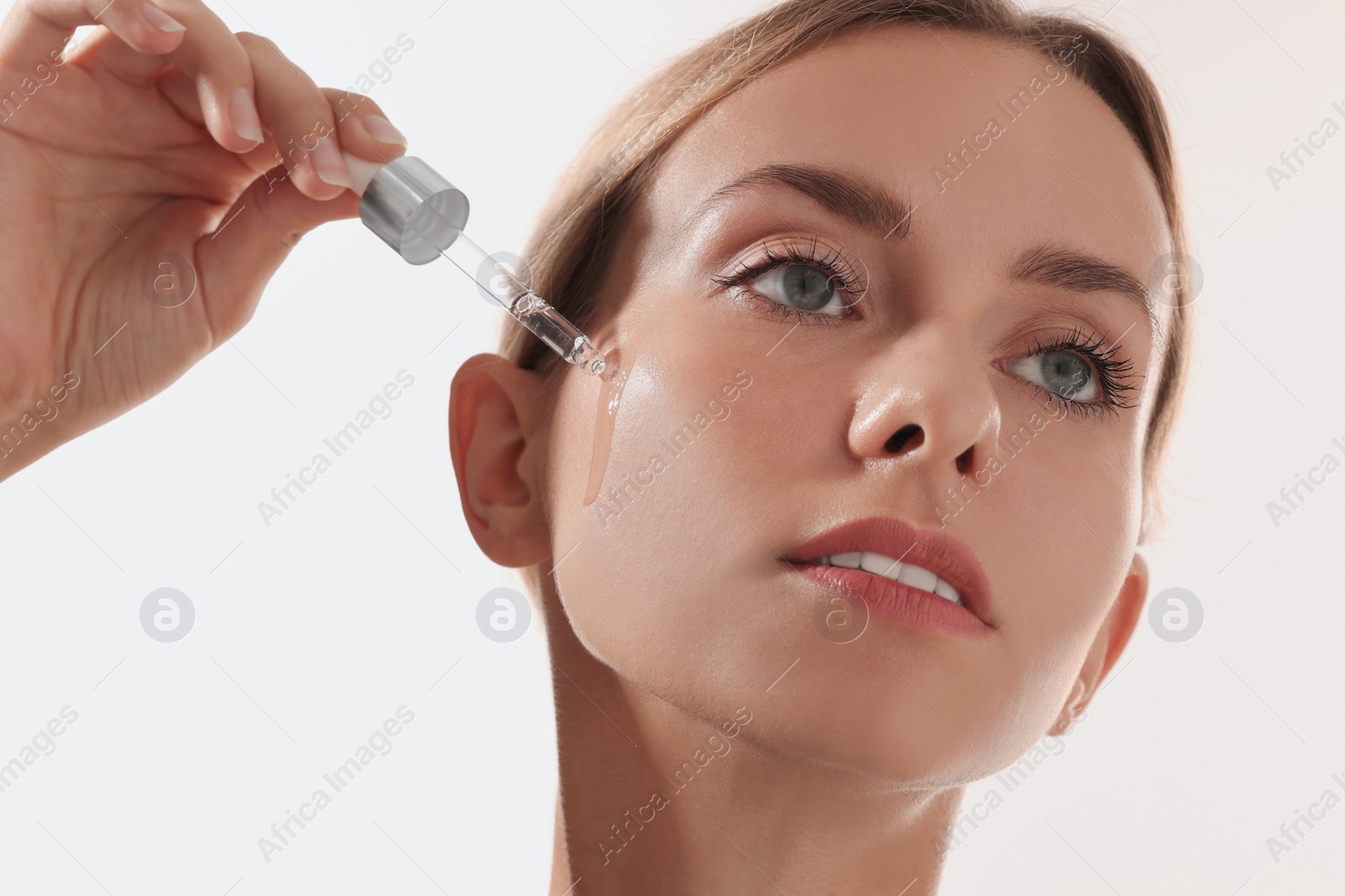 Photo of Beautiful woman applying cosmetic serum onto her face on white background