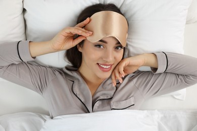 Photo of Beautiful young woman with sleeping mask lying in bed, top view