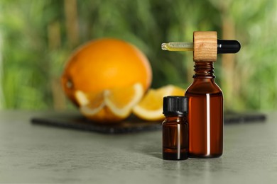 Photo of Bottles of citrus essential oil and pipette on grey table, space for text