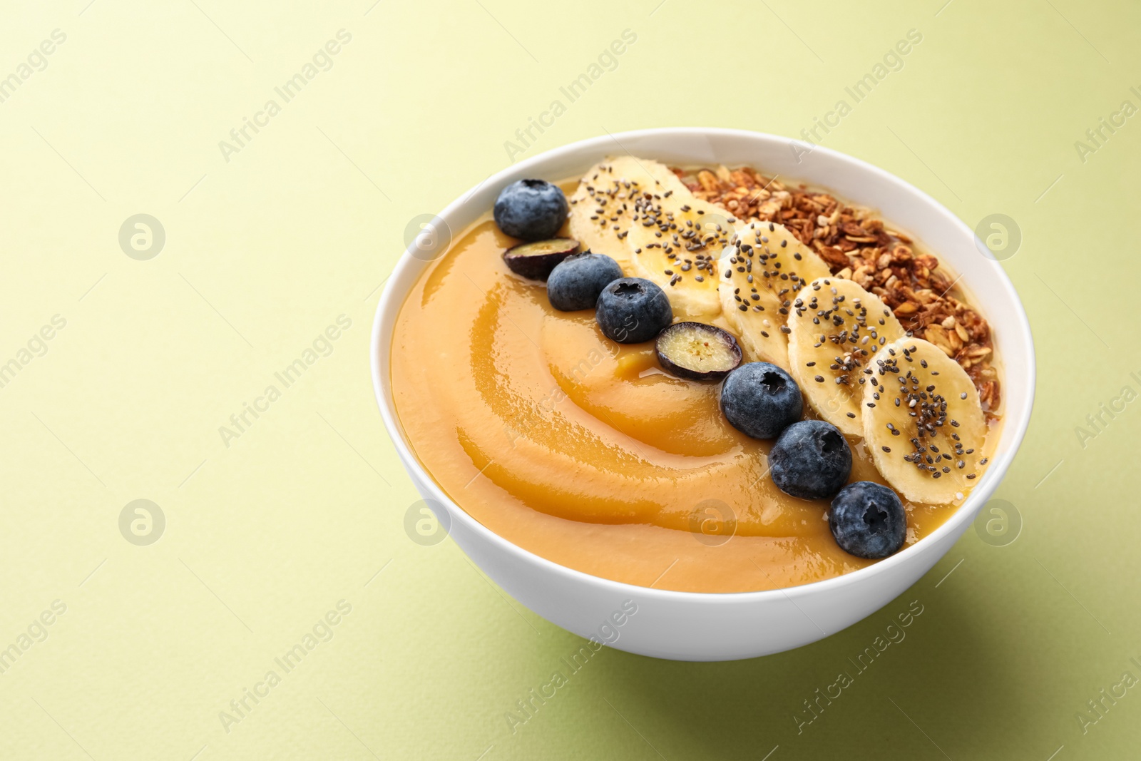 Photo of Delicious smoothie bowl with fresh blueberries, banana and granola on pale olive background