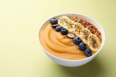 Delicious smoothie bowl with fresh blueberries, banana and granola on pale olive background