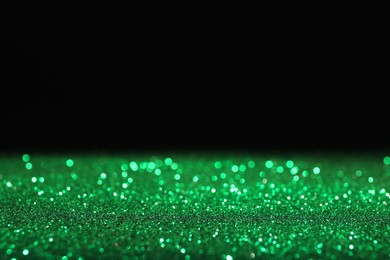 Photo of Shiny green glitter on black background, space for text. Bokeh effect