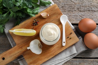 Photo of Fresh mayonnaise sauce in glass jar and ingredients on wooden table, flat lay