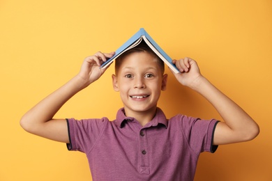 Photo of Portrait of cute boy with book on yellow background. Reading concept