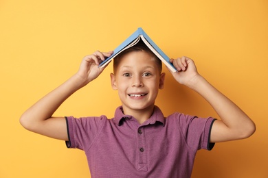 Portrait of cute boy with book on yellow background. Reading concept