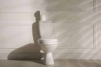 Photo of Modern toilet bowl and paper rolls near white wall in restroom. Interior design