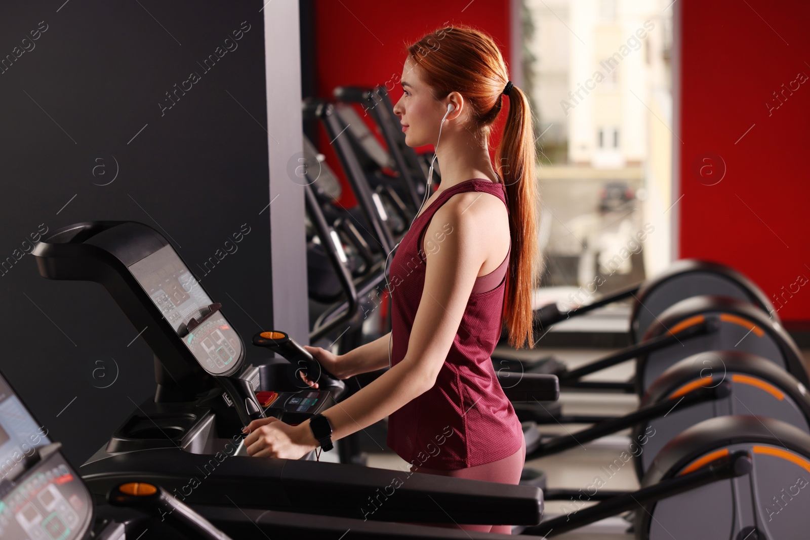 Photo of Athletic young woman with earphones training on treadmill in gym