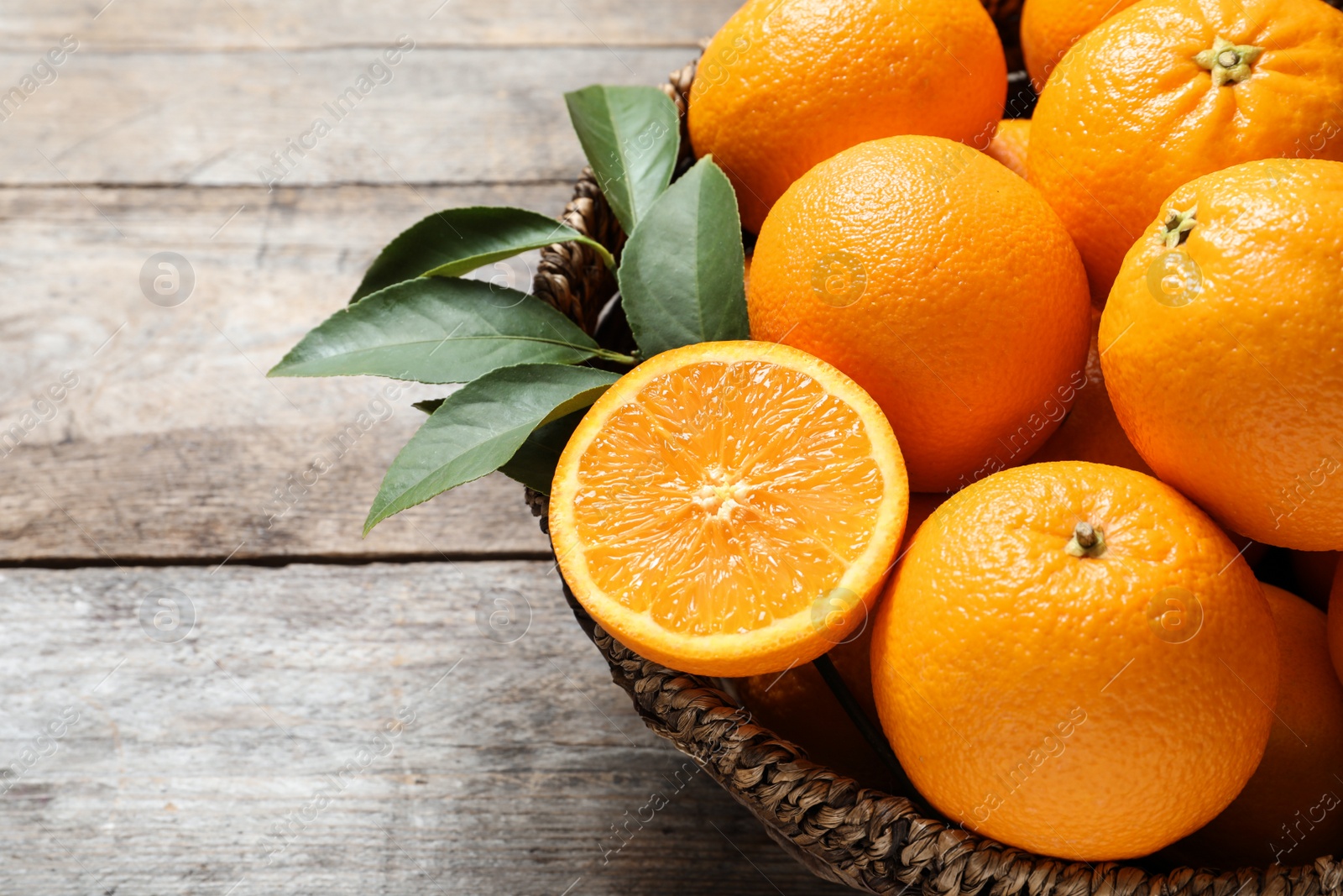 Photo of Wicker bowl with ripe oranges on wooden background, closeup. Space for text