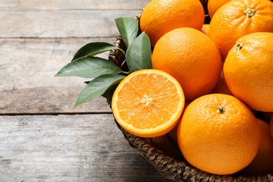 Wicker bowl with ripe oranges on wooden background, closeup. Space for text