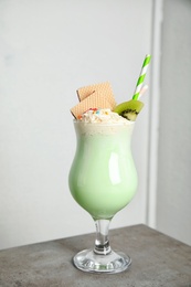 Glass with delicious milk shake on table against light background