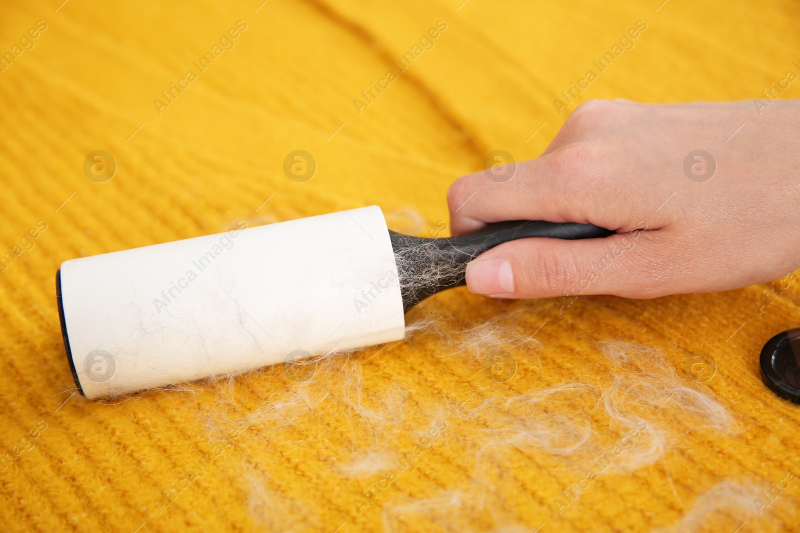 Photo of Woman removing hair from yellow knitted jacket with lint roller, closeup