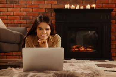 Photo of Young woman with laptop on floor near fireplace at home