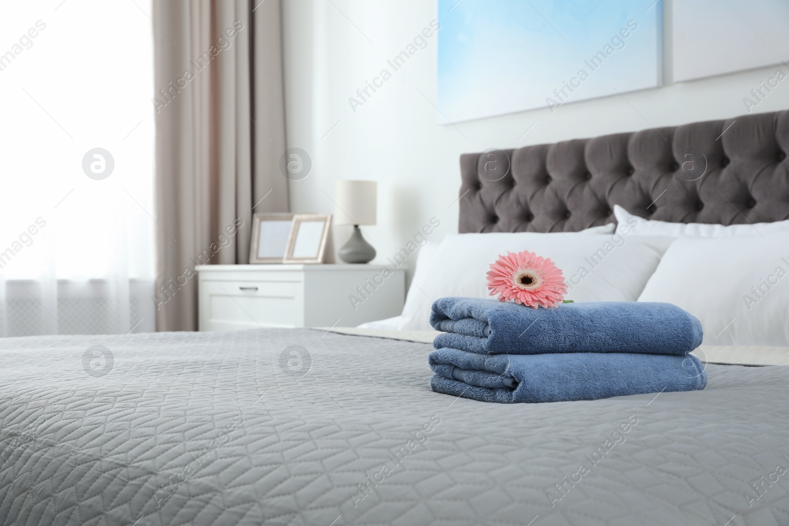 Photo of Stack of clean towels with flower on bed indoors. Space for text