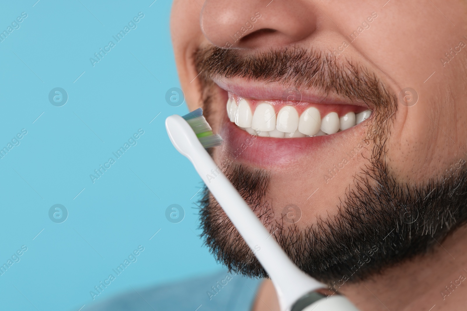 Photo of Man brushing his teeth with electric toothbrush on light blue background, closeup. Space for text