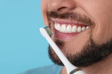 Photo of Man brushing his teeth with electric toothbrush on light blue background, closeup. Space for text