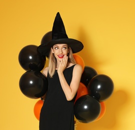 Photo of Beautiful woman wearing witch costume with balloons for Halloween party on yellow background, space for text