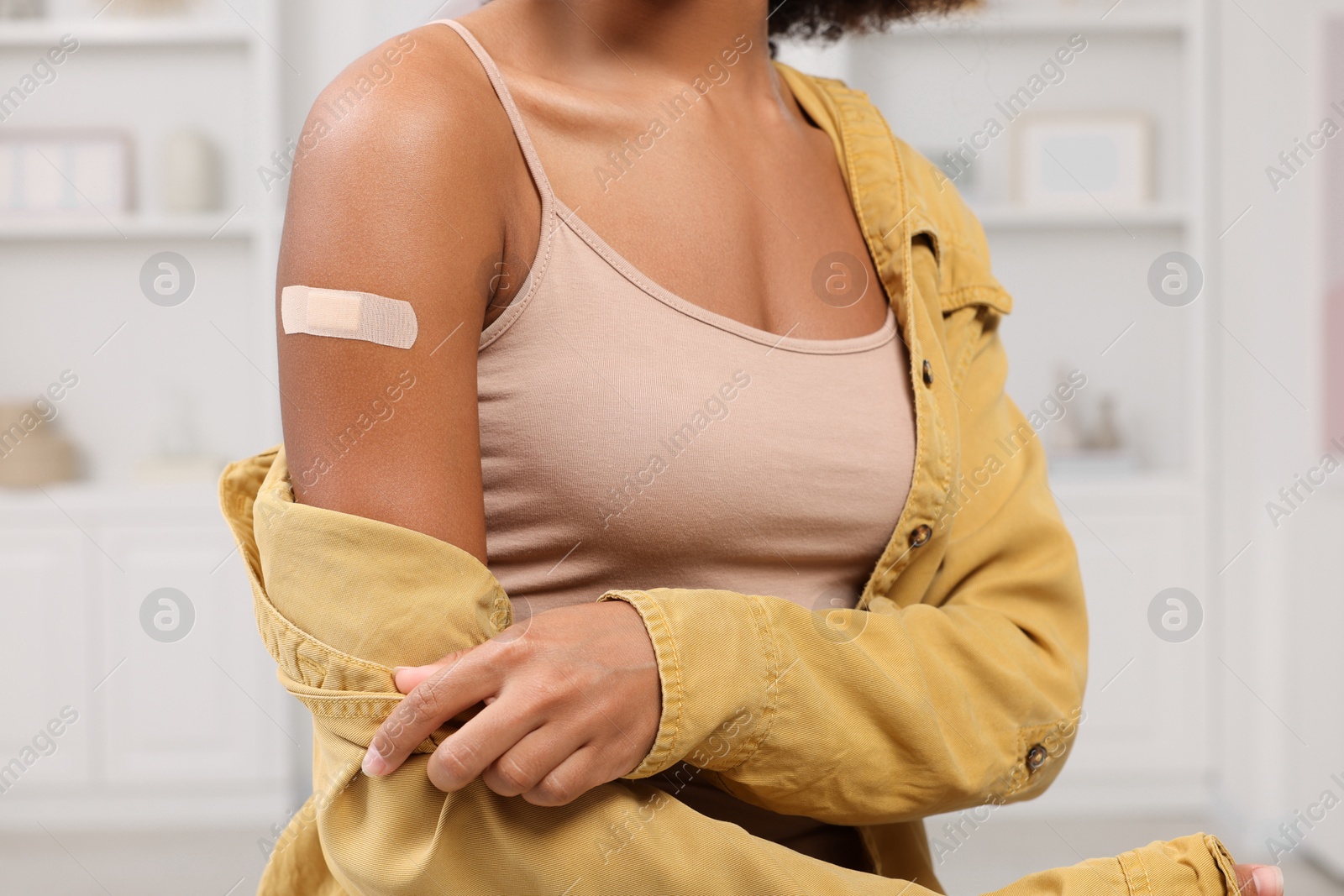 Photo of Young woman with adhesive bandage on her arm after vaccination indoors, closeup