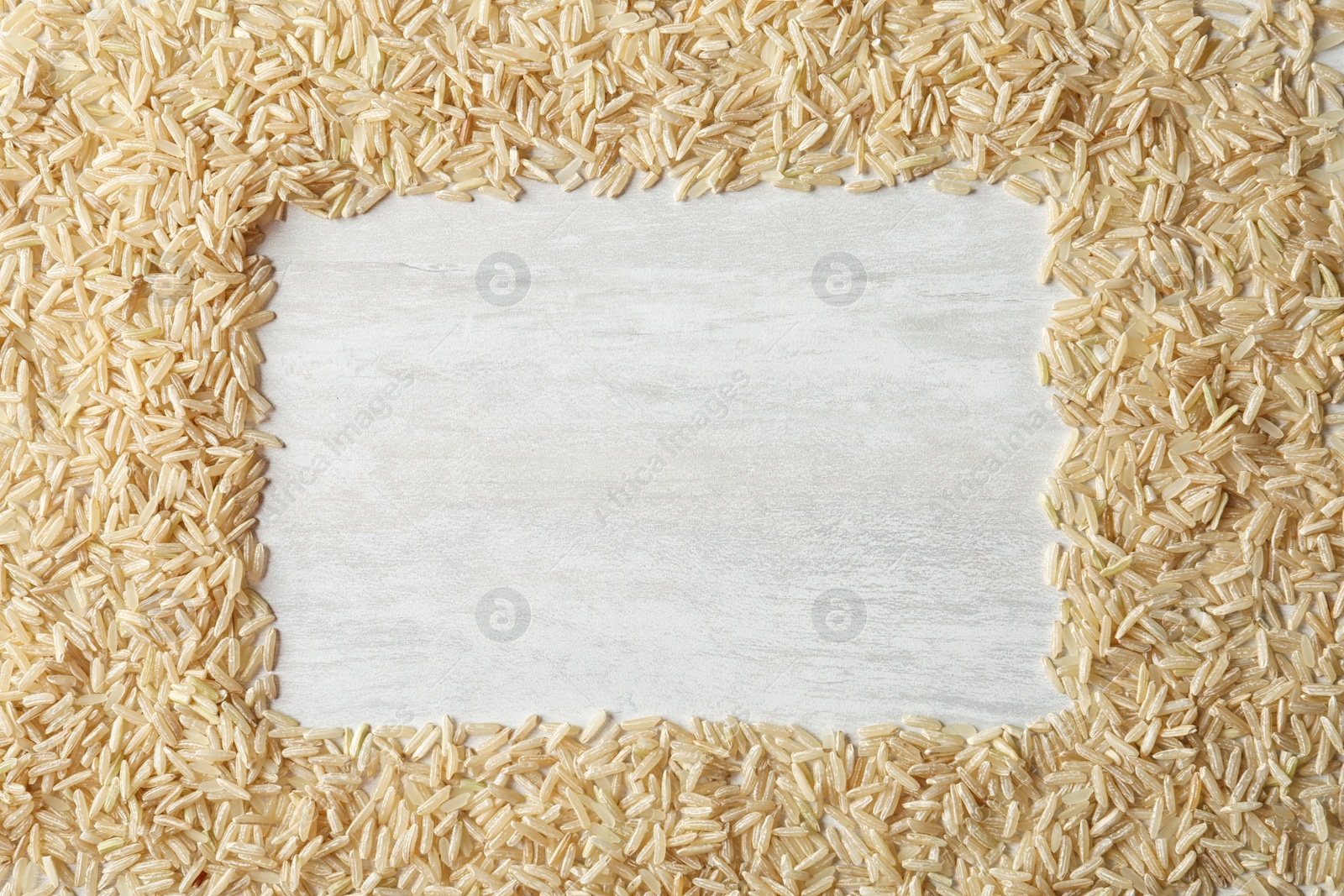 Photo of Frame made with brown rice on white wooden background, top view. Space for text