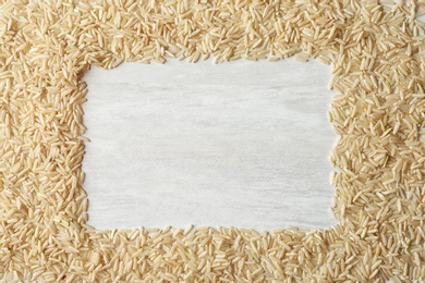 Frame made with brown rice on white wooden background, top view. Space for text