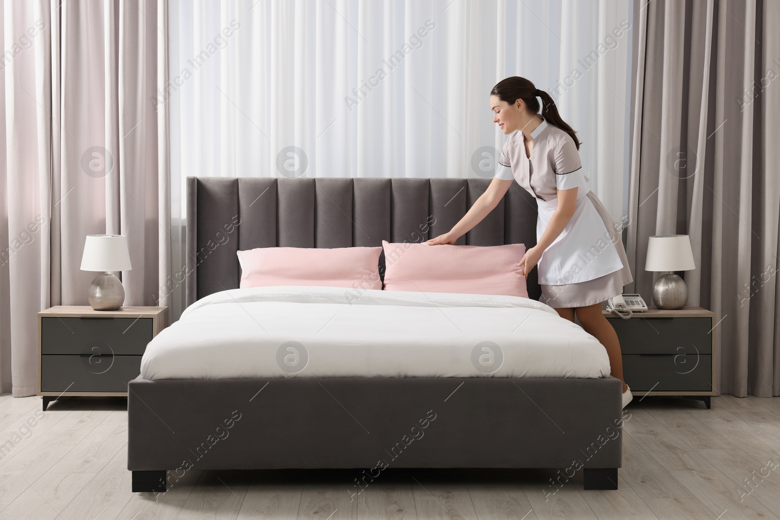 Photo of Young maid making bed in hotel room