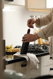 Man opening wine bottle with corkscrew at countertop indoors, closeup