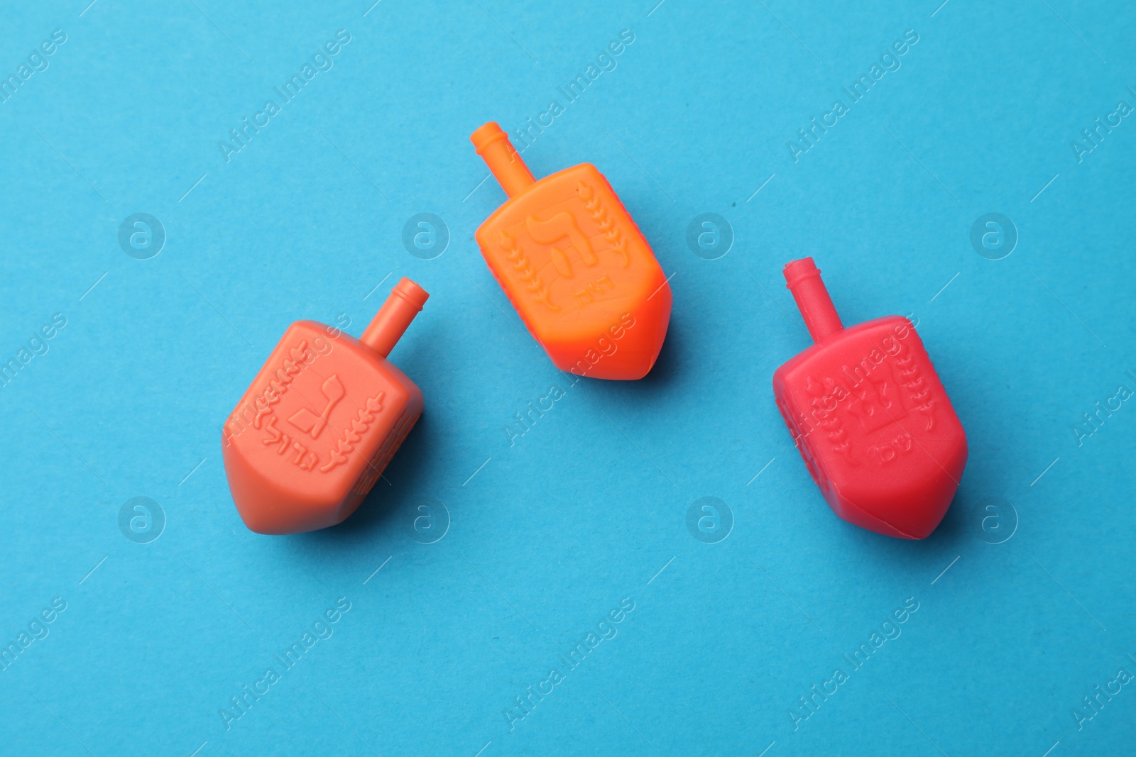 Photo of Colorful dreidels on light blue background, flat lay. Traditional Hanukkah game