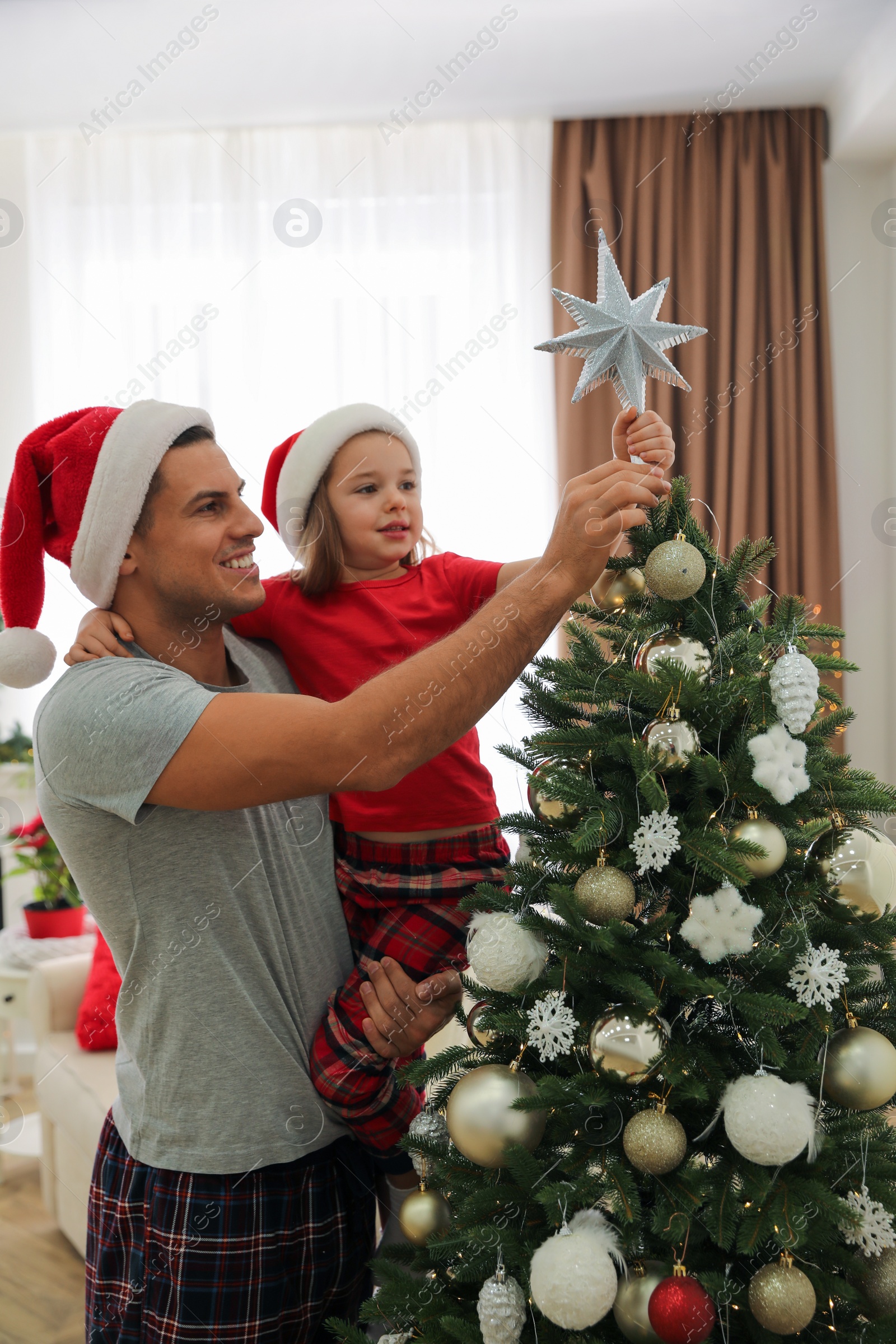 Photo of Father and little daughter decorating Christmas tree with star topper indoors