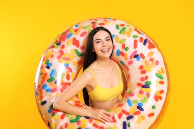 Happy young woman with beautiful suntan and inflatable ring against orange background