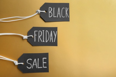Photo of Tags with words BLACK FRIDAY SALE on golden background, flat lay. Space for text