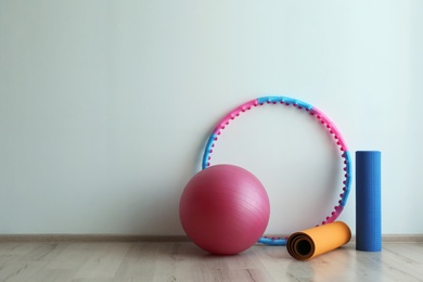 Photo of Hula hoop, fitness ball and mats near light wall in gym. Space for text