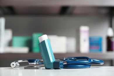 Asthma inhaler and stethoscope on table against blurred background