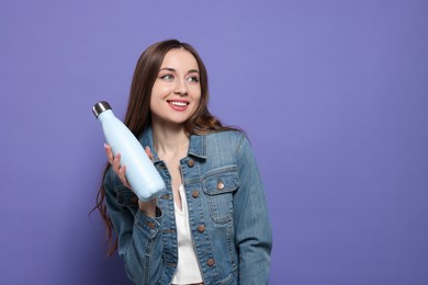 Photo of Beautiful young woman with thermos bottle on purple background, space for text