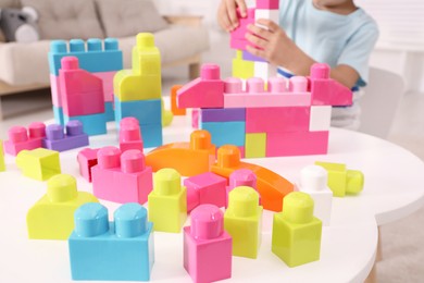 Little child playing with colorful building blocks at table indoors, closeup