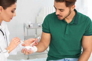 Female doctor applying bandage on young man's hand in clinic. First aid