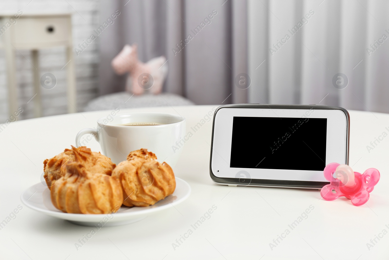 Photo of Modern monitor, cup of coffee, cookies and pacifier on table indoors, space for text. CCTV equipment