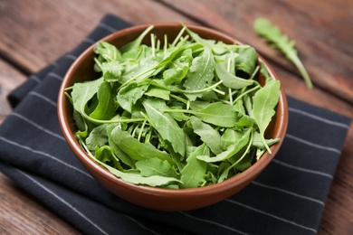 Photo of Fresh arugula leaves in bowl on wooden table, closeup