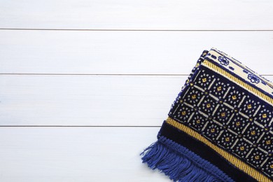 Photo of Muslim prayer rug on white wooden table, top view. Space for text