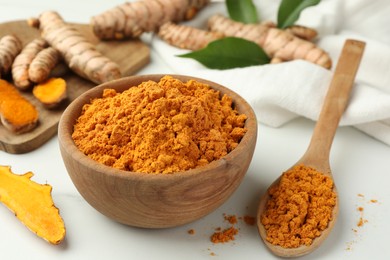 Photo of Aromatic turmeric powder and raw roots on white table, closeup