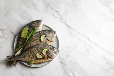 Photo of Seafood. Delicious baked fish served with green onion and lime on white marble table, top view. Space for text