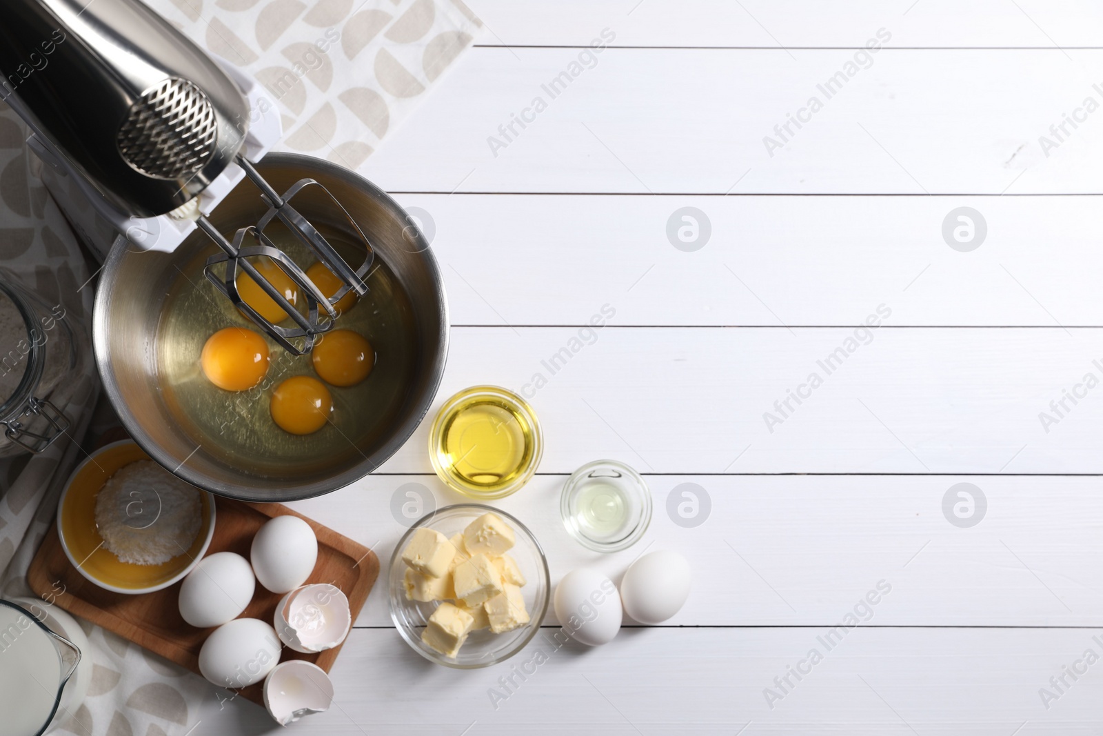 Photo of Making dough. Raw eggs in bowl of stand mixer and ingredients on white wooden table, flat lay with space for text