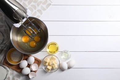 Photo of Making dough. Raw eggs in bowl of stand mixer and ingredients on white wooden table, flat lay with space for text