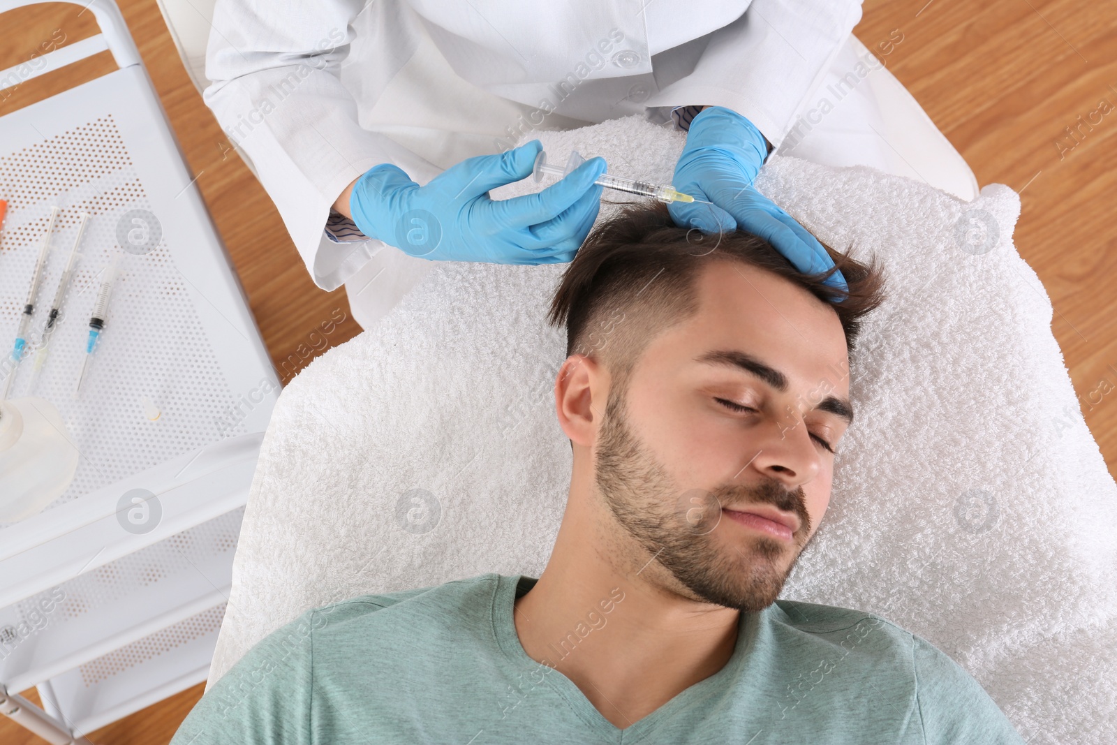Photo of Young man with hair loss problem receiving injection in salon, top view