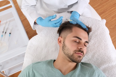 Young man with hair loss problem receiving injection in salon, top view