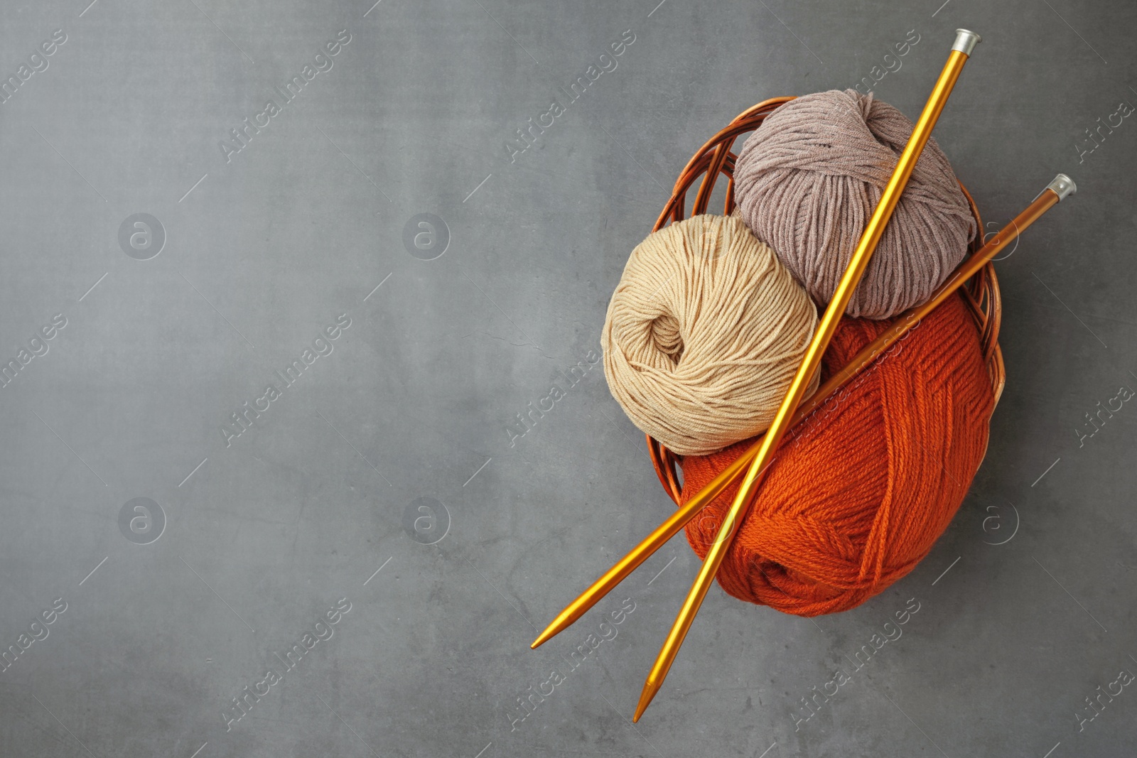 Photo of Different balls of woolen knitting yarns and needles on grey background, top view. Space for text
