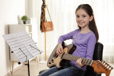 Photo of Little girl playing guitar at music lesson. Learning notes