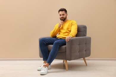 Photo of Handsome man sitting in armchair near beige wall indoors