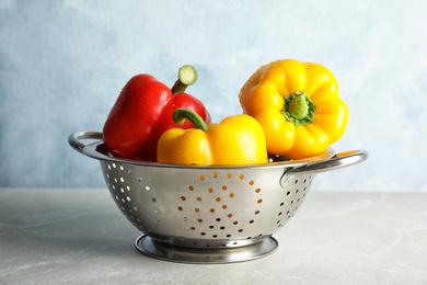 Colander with ripe paprika peppers on table