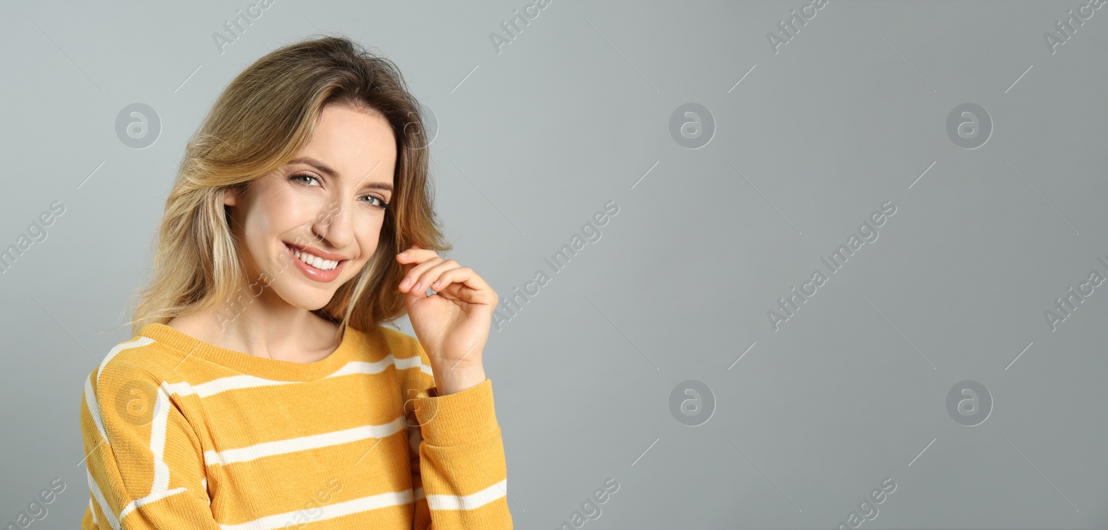 Photo of Portrait of happy young woman with beautiful blonde hair and charming smile on grey background