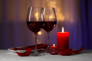 Photo of Romantic table setting with glasses of red wine and burning candles against blurred lights